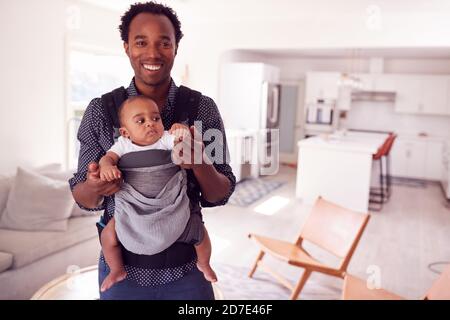 Portrait Of Father Playing With Smiling Baby Daughter In Sling At Home Stock Photo