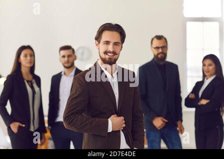 Young business leader or company manager in formal suit with team of office workers in background Stock Photo