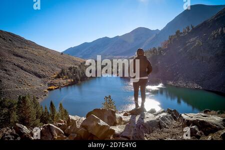 MONO COUNTY, CALIFO, UNITED STATES - Oct 17, 2020: A solo female hiker stands on a rock promontory over Blue Lake in the Eastern Sierra's Virginia Lak Stock Photo