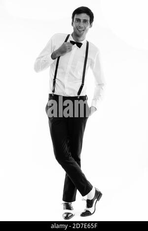 Full body shot of young happy man smiling while wearing suspenders and holding bow tie Stock Photo