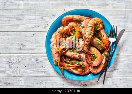 Garlic butter jumbo shrimps cooked on a skillet with lime and fresh parsley of big size whole pink shrimps served on a blue plate on a wooden backgrou Stock Photo