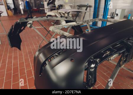 Auto bumper part is installed on the racks after painting in car repair shop. Stock Photo