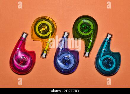 Multi colored correction tape dispensers flat lay design centered on a plain orange cardstock background. Stock Photo