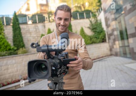 Fair-haired cameraman standing behind camera, getting ready for filming Stock Photo