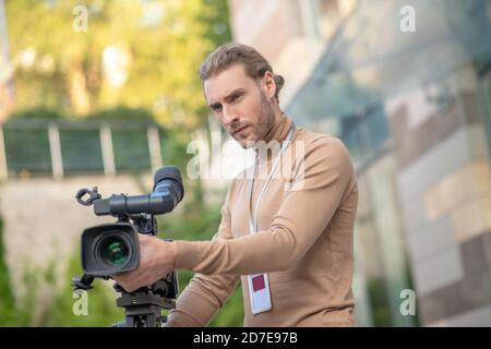 Concentrated cameraman standing behind camera, getting ready for filming Stock Photo