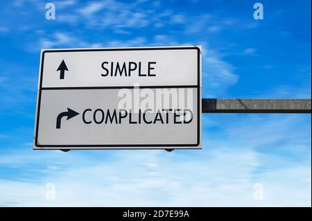 Simple versus complicated. White two street signs with arrow on metal pole. Directional road. Crossroads Road Sign, Two Arrow. Blue sky background. Stock Photo