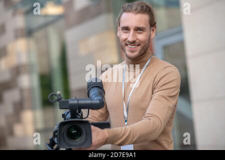 Smiling fair-haired cameraman standing behind camera, posing Stock Photo