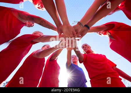 Low Angle View Of Manager Joining Hands With Womens Soccer Team During Pep Talk Before Match Stock Photo