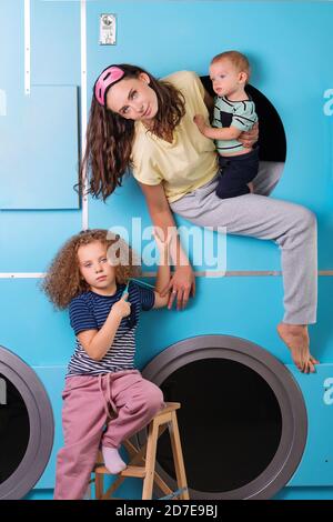 Mother Household With Children Wearing Pyjamas Having Fun And Doing Laundry At Self Service Laundrette Near Washing Machines Stock Photo