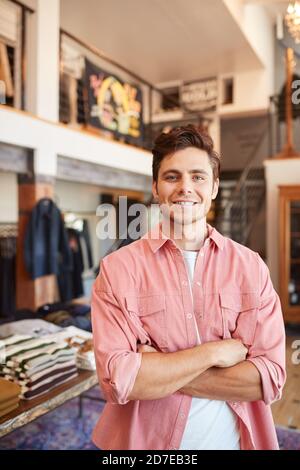 Portrait Of Smiling Male Owner Of Fashion Store Standing In Front Of Clothing Display Stock Photo