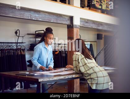 Two Female Fashion Designers Having Creative Meeting Around Wooden Table In Studio Stock Photo