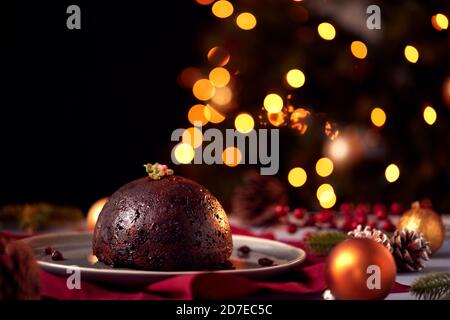 Traditional Christmas Pudding On Table Set For Festive Christmas Meal With Tree Lights In Background Stock Photo