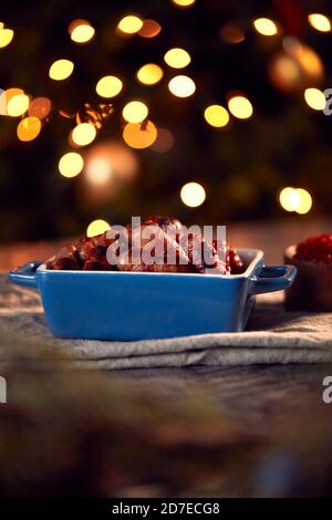 Traditional Dish Of Christmas Pigs In Blankets On Table Set For Meal With Tree Lights In Background Stock Photo