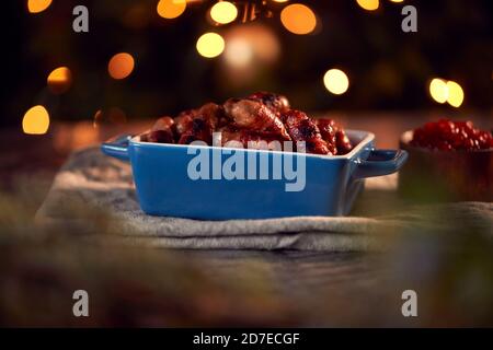 Traditional Dish Of Christmas Pigs In Blankets On Table Set For Meal With Tree Lights In Background Stock Photo