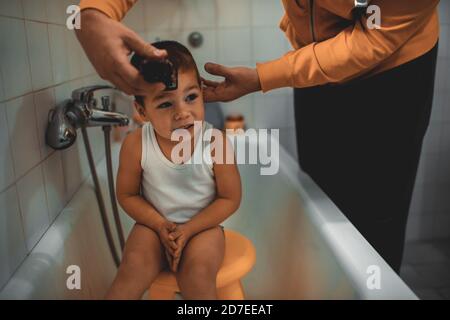 Father cutting son's hair at home during the 2020 pandemic lockdown. Covid-19 social distancing Stock Photo