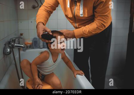 Father cutting son's hair at home during the 2020 pandemic lockdown. Covid-19 social distancing Stock Photo