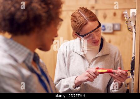 Female Tutor With Trainee Electrician In Workshop Studying For Apprenticeship At College Stock Photo