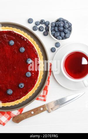 Homemade cheesecake with berry jelly and cup of red tea hibiscus on white wooden table. Top view. Stock Photo