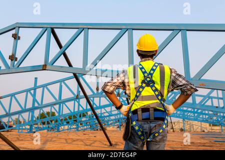 The back of construction worker wearing safety harness and safety line working at high place on roof in construction site. Stock Photo