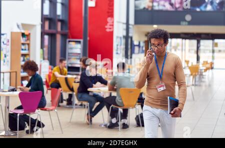 Communal Area Of Busy College Campus With Students Working At Tables And Tutor On Phone Stock Photo