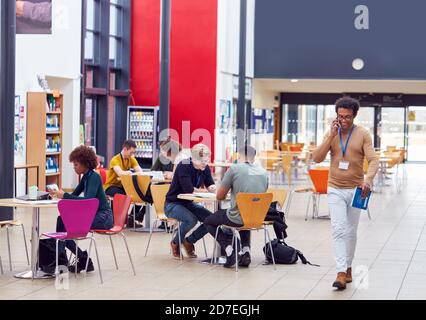 Communal Area Of Busy College Campus With Students Working At Tables And Tutor On Phone Stock Photo