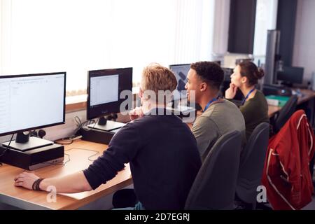 Group Of College Students Studying Computer Design Sitting At Line Of Monitors In Classroom Stock Photo
