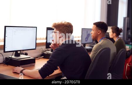 Group Of College Students Studying Computer Design Sitting At Line Of Monitors In Classroom Stock Photo