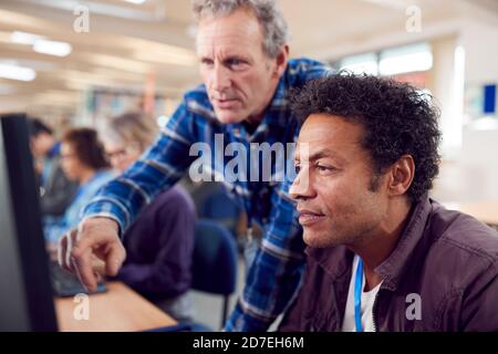 Teacher With Group Of Mature Adult Students In Class Working At Computers In College Library Stock Photo