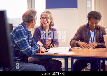 Teacher With Mature Female Adult Student Using Mobile Phone At Table Working In College Library Stock Photo