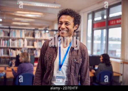 Portrait Of Mature Male Teacher Or Student In Library With Other Students Studying In Background Stock Photo
