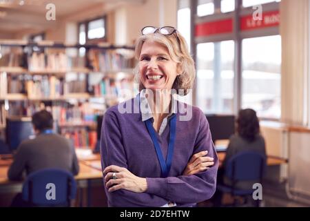 Portrait Of Mature Female Teacher Or Student In Library With Other Students Studying In Background Stock Photo