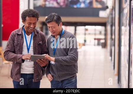 Two Mature Male Students Or Teachers With Digital Tablet Walk Through Hall Of College Building Stock Photo