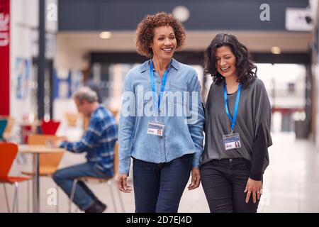 Two Mature Female Students Or Teachers Walking Through Communal Hall Of Busy College Campus Building Stock Photo
