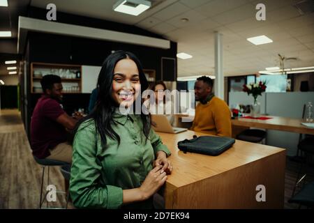 Portrait of Indian business woman smiling taking lunch break while colleagues prepare for meeting with partners  Stock Photo