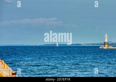 A lonely sailing boat in Aarhus harbour sails in a calm Baltic sea beside Arhus Lighthouse inspiring a romantic escape or team sport activity Stock Photo