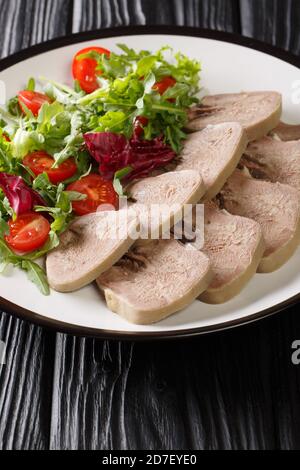 Boiled chopped beef tongue with fresh salad close-up in a plate on the table. vertical Stock Photo