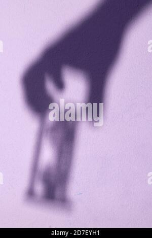 Shadow of a hand holding an hourglass. Sand clock in a hand - shadow on the wall. Stock Photo