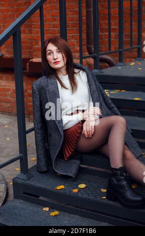 Tired woman in elegant fashionable clothes sitting on a mettalic steps of her house porch. Apathy concept. Stock Photo
