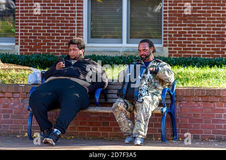 Frederick, MD 10/13/2020: Two African American men living on streets are sitting on a bench in a park in Frederick, Maryland. Homeless people have old Stock Photo