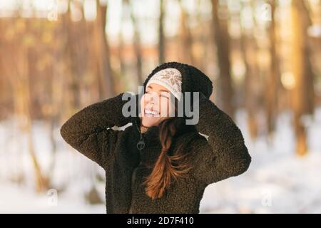 Winter snow fun happy girl walking outside in cold weather protecting ears holding wool hat over ears active outdoor lifestyle. Asian girl wearing Stock Photo