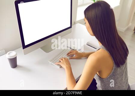 Asian woman working on computer with blank white screen sitting at desk in office Stock Photo