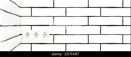 Electrical outlets against a white brick wall. Space for text. Stock Photo
