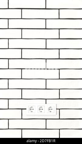 Electrical outlets against a white brick wall. Space for text. Stock Photo