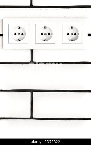 Electrical outlets against a white brick wall. Space for text. Stock Photo