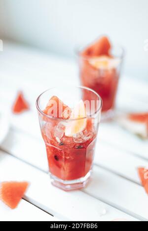 Fresh watermelon refreshing summer cocktail smoothie with lemon and ice in glass jar on white wooden board Stock Photo