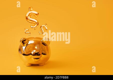 Golden piggy bank on yellow background with Gold USD Sign Balloons. Golden currency symbol made of inflatable foil balloon. Investment and banking Stock Photo