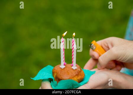 hand with a lighter to light the candle blueberry muffins on green background. burning four candles on Birthday cupcake.Anniversary celebration. Stock Photo