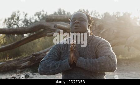 oung african man meditationg or praying in front of the old tree trunk. High quality photo Stock Photo