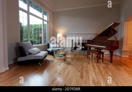 Newly remodeled large living room with glowing fireplace and piano on red oak wood floors Stock Photo