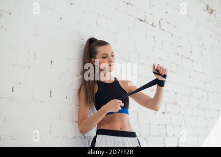 At the beginning of the workout, a pretty kickboxer girl prepares her hands by wrapping a bandage Stock Photo